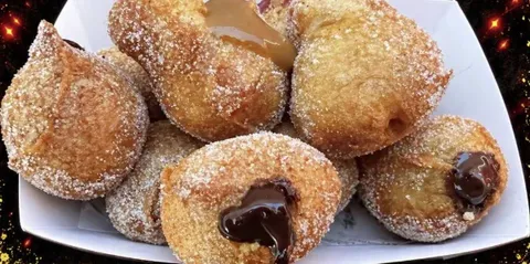 A tray of little sugar dusted doughnut balls with chocolate and caramel fillings